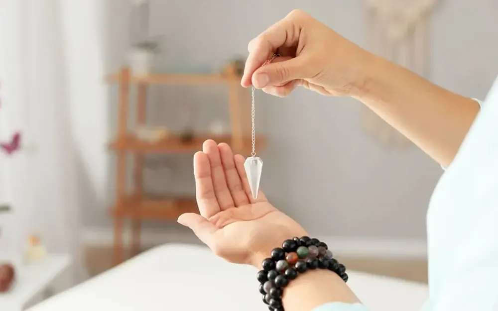 Person holding a pendulum over a tarot card spread to achieve clarity in readings